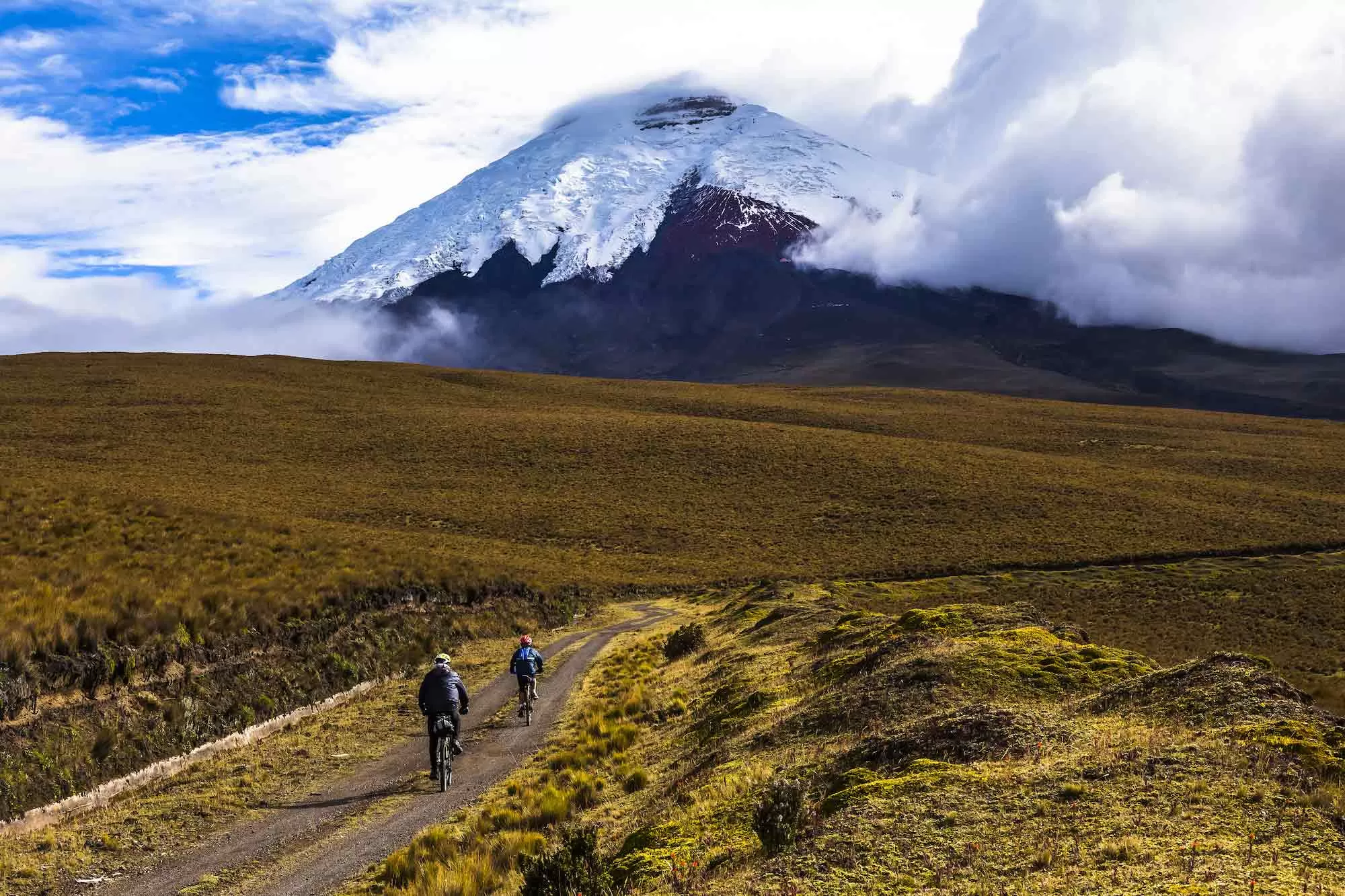 Cotopaxi volcano in Cotopaxi National Park, Ecuador, with two people mountain biking on a trail.