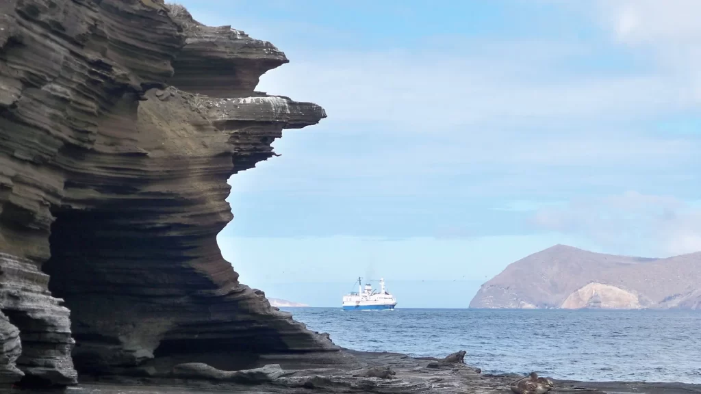 Unique rock formations along the coast of Puerto Egas, Santa Cruz Island, with a boat visible in the background.