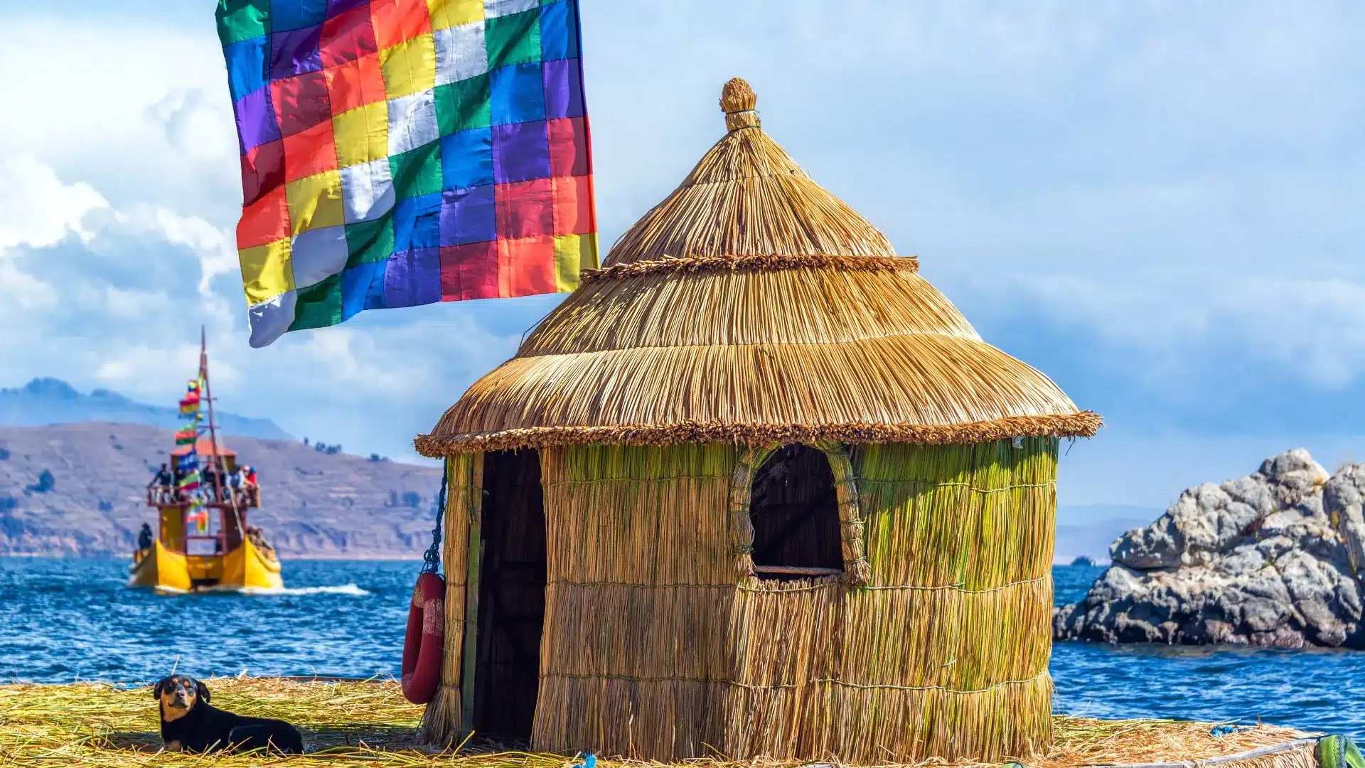 Traditional totora reed house on the Uros Floating Islands, with the Wiphala flag waving above Lake Titicaca.