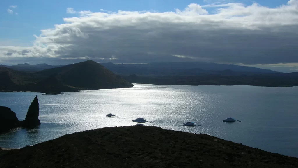 Blue ocean and sky around Bartolomé Island, Galápagos, with boats appearing as silhouettes among the surrounding islands.