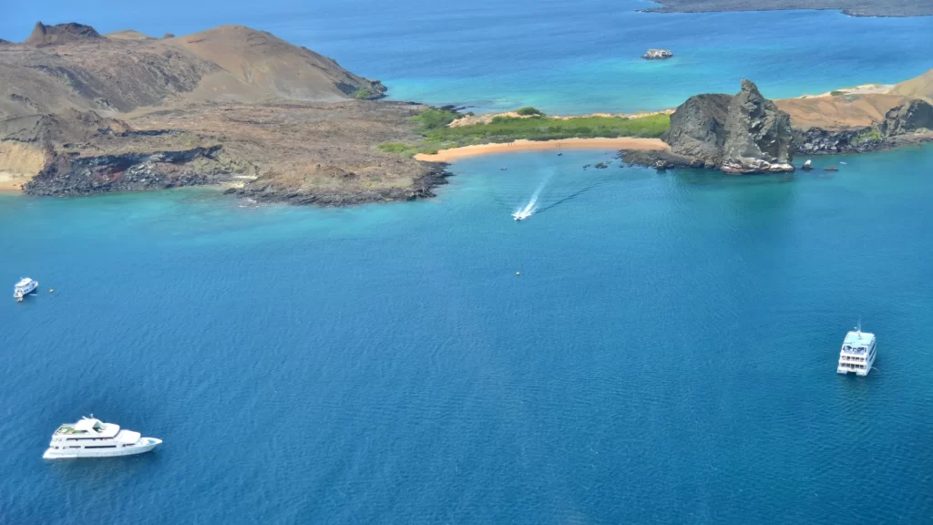 A distant view of Bartolomé Island in the Galápagos, with a few boats sailing across the open ocean.