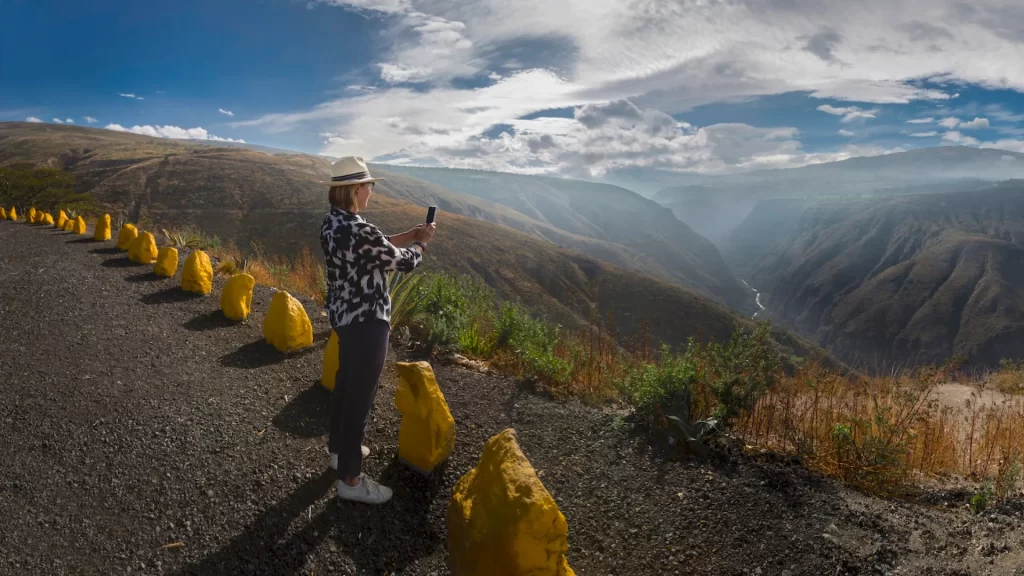 A person taking a photo from a scenic viewpoint overlooking a deep canyon in the Andes near Guayllabamba, Ecuador.