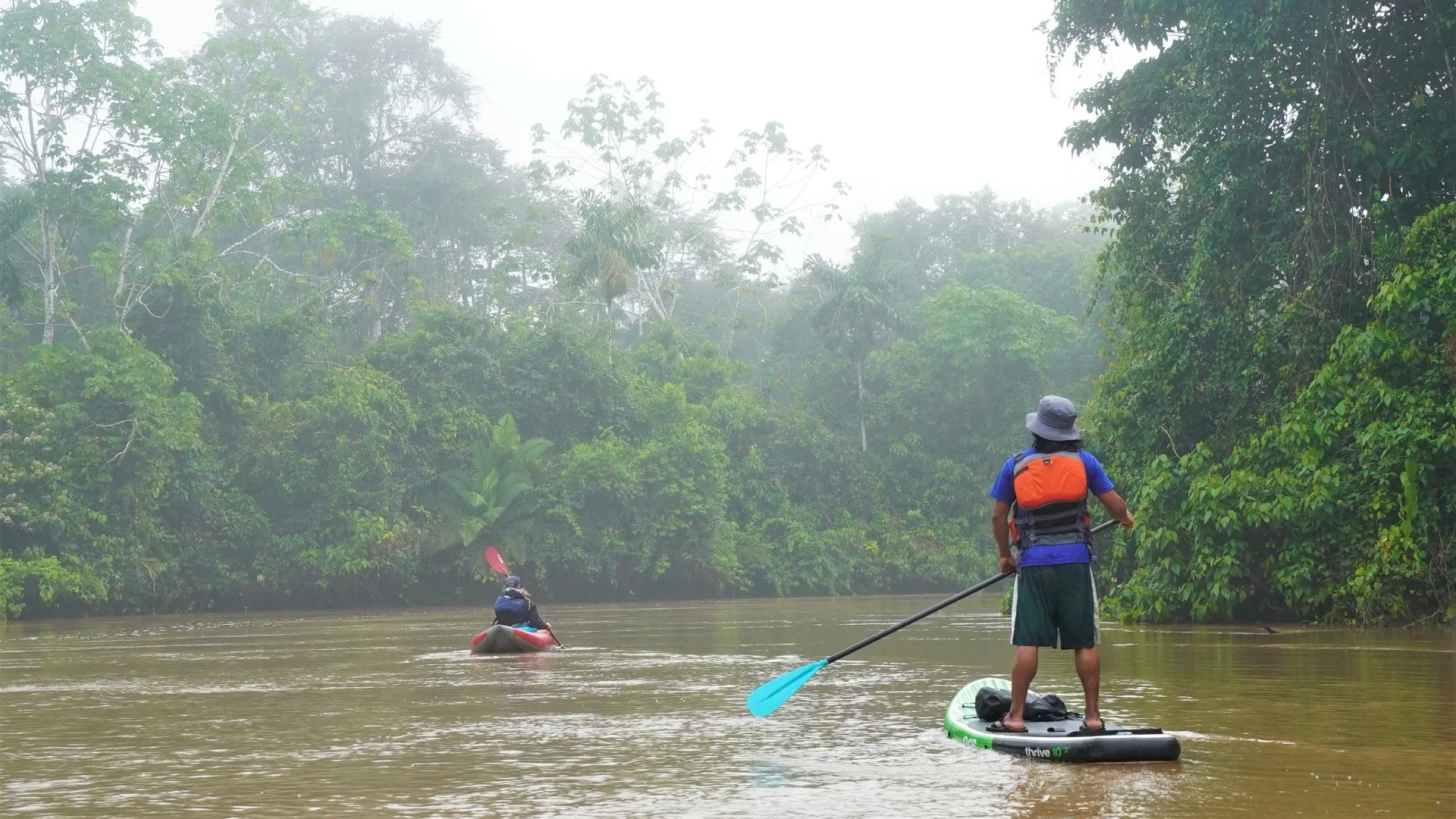 Two people navigating the Shiripuno River in Yasuni Biosphere Reserve, Ecuador, on a stand-up paddleboard and a kayak.