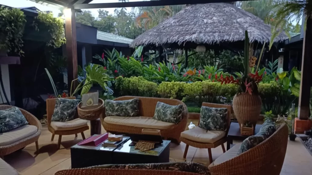 Outdoor lounge with rattan furniture, tropical plants, and thatched-roof cabana at Amazon Bed & Breakfast, Leticia.