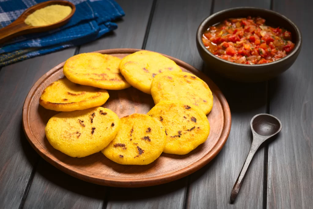 Traditional Colombian arepas served on a wooden plate with hogao tomato and onion sauce on the side.