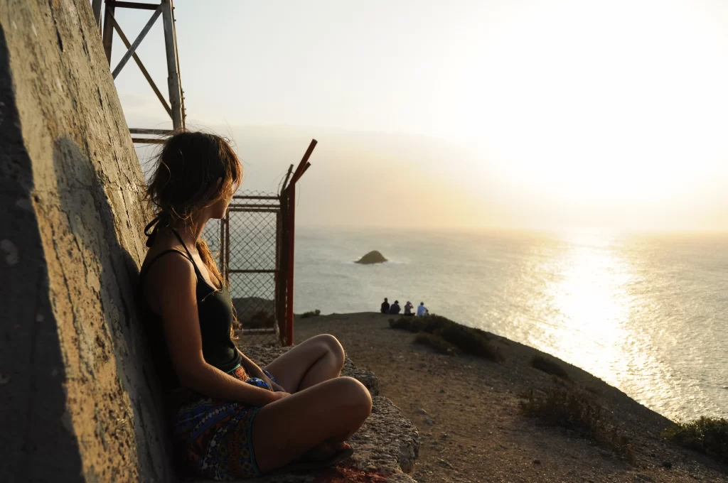 Traveler sitting by the coast at sunset in La Guajira, Colombia, watching the golden light reflect on the sea.