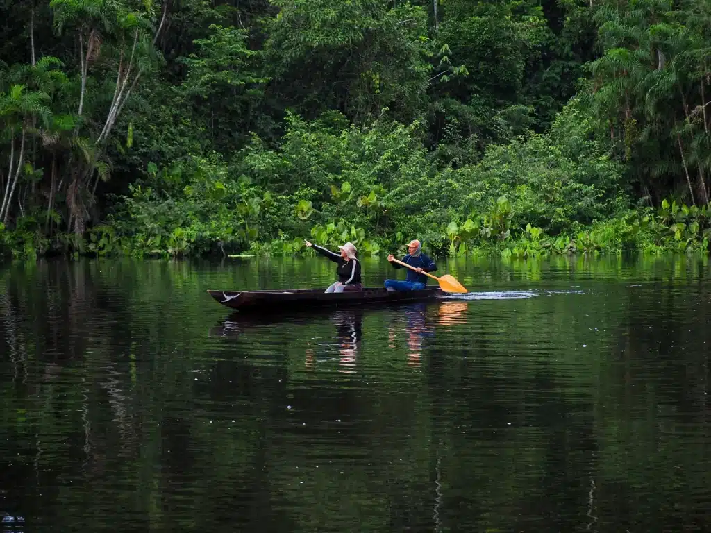 Tourists in a motorized canoe pointing at wildlife along the banks of the Zábalo River, Cuyabeno Reserve, Ecuador.