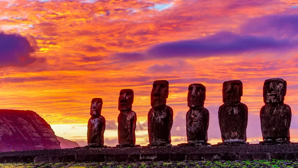 Easter Island stone giants standing on an ahu at sunset, facing the Pacific Ocean.